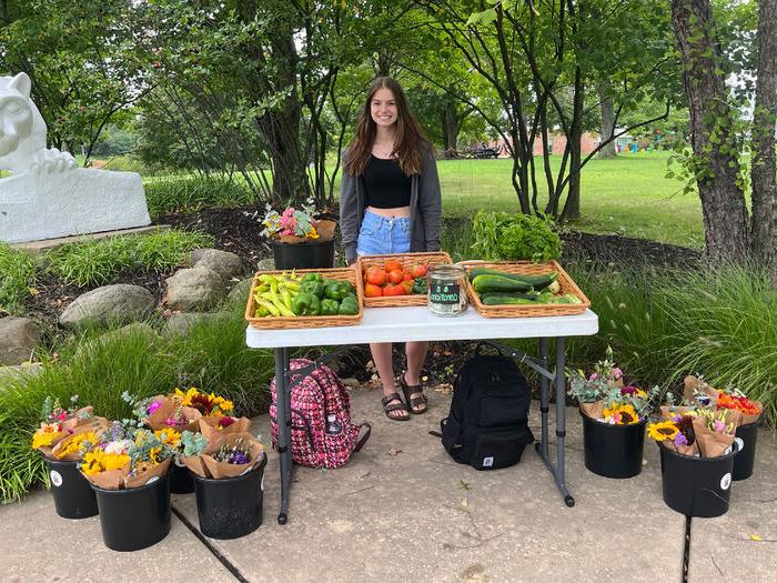 A female student stands behind a table loaded with fresh-cut flowers